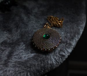 Vintage Bismarckhalsband med rund medaljong och grön sten på grå päls.