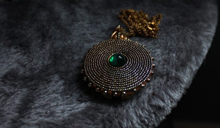 Vintage Bismarckhalsband med rund medaljong och grön sten på grå päls.