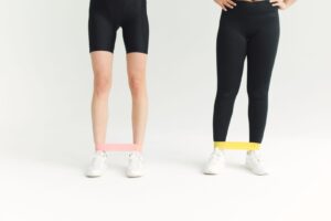 Två personer som tränar hemma med gummiband runt vristerna.