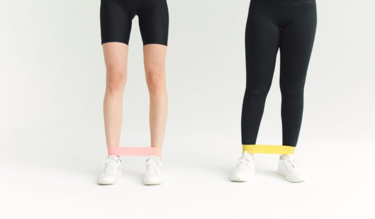 Två personer som tränar hemma med gummiband runt vristerna.