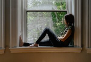 Person sitter i ett fönster och blickar ut mot grönskan