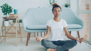Person sitter i korslagd meditationsställning i ett ljust vardagsrum