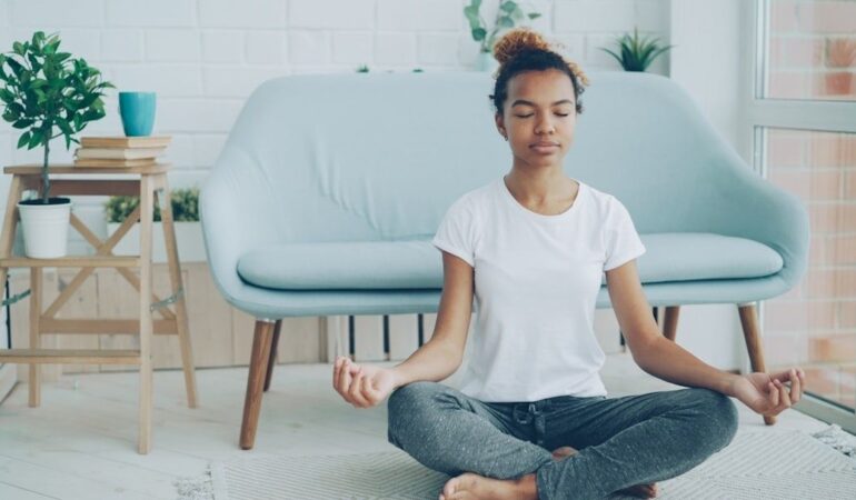 Person sitter i korslagd meditationsställning i ett ljust vardagsrum